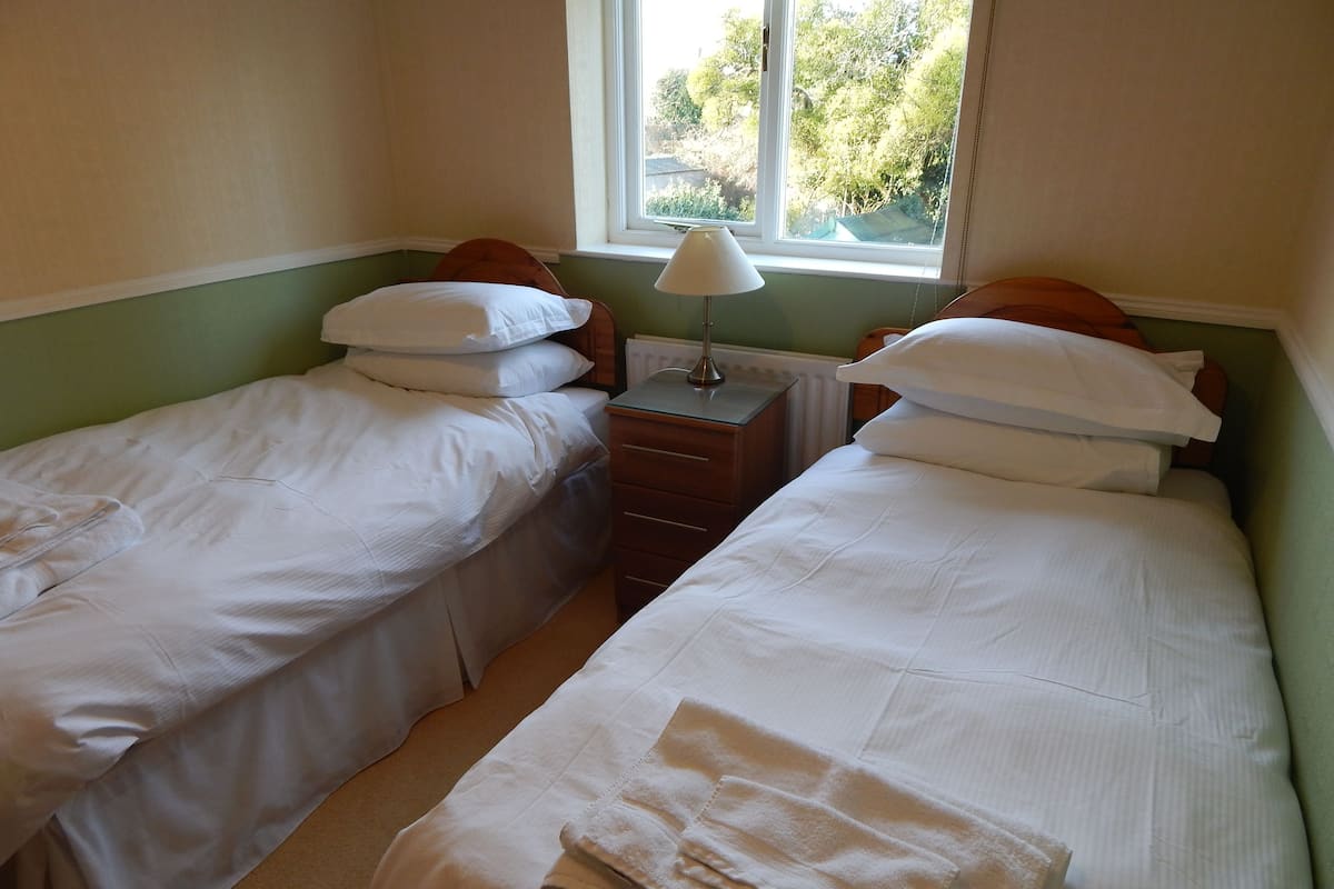 A twin room with two single beds, a nightstand with a lamp, and a window with a view of trees.