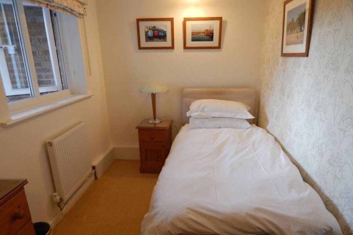 A bedroom with a bed, a nightstand, a lamp, a dresser, and a radiator.