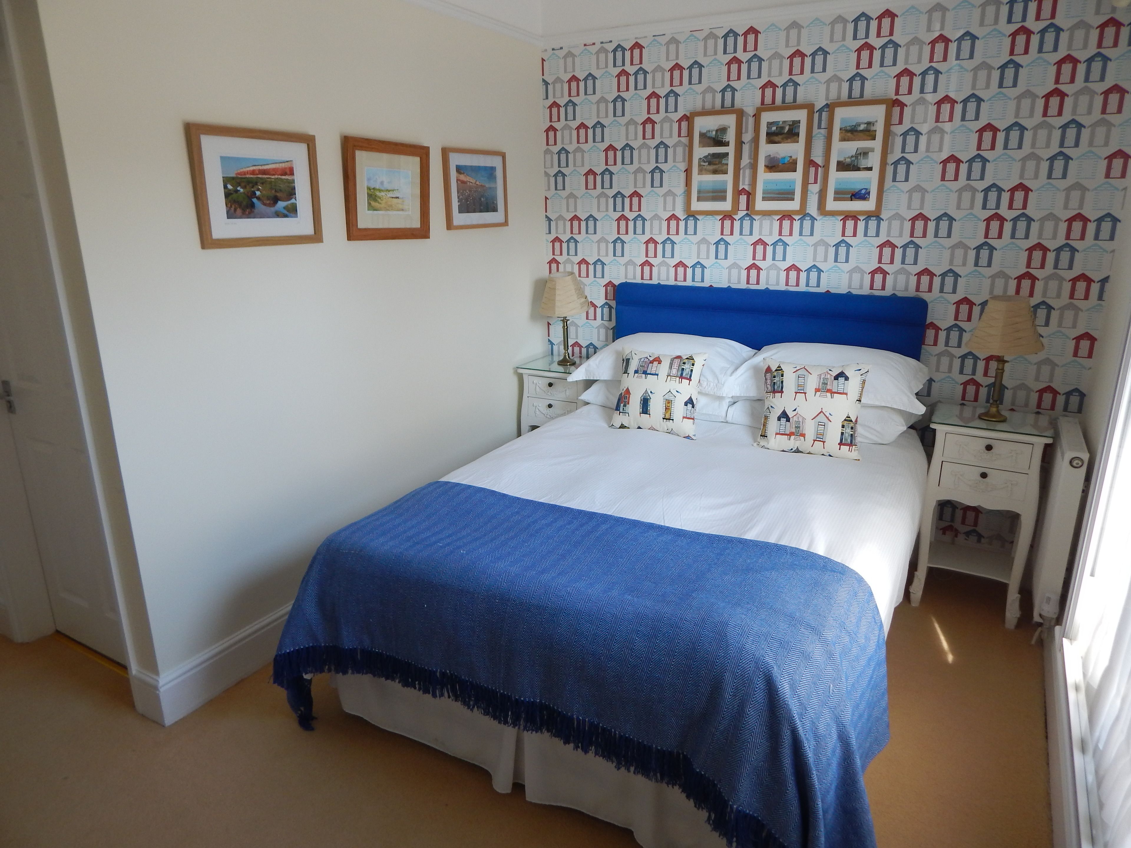 A neatly made bed with a blue headboard, white bedding, and matching pillows. There are three framed pictures on the wall above the bed.
