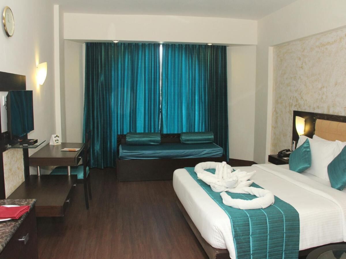 Habitación de hotel con cama, escritorio, silla, televisor y cortina.