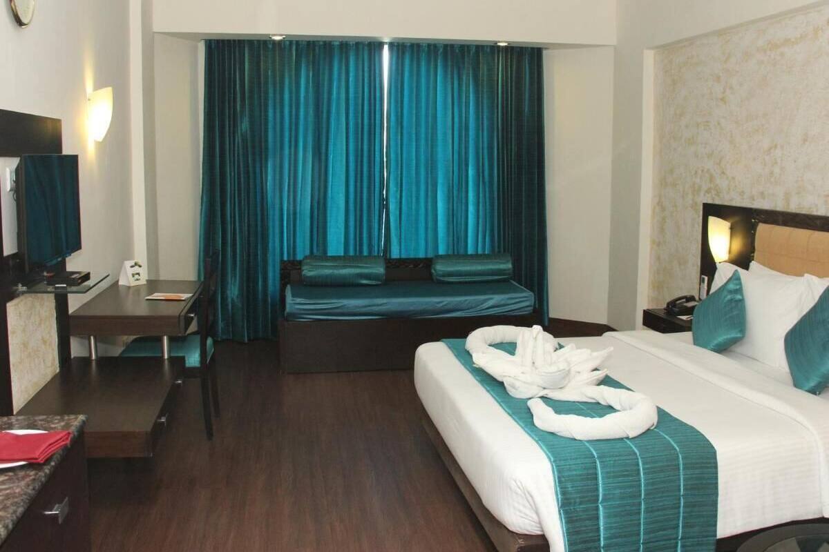 A hotel room with a bed, a desk, a chair, a TV, and a curtain.