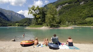 A lakeside scene with people relaxing on the shore, a boat, and a clear view of the surrounding mountains. - Hotel Antica Croce (Tenno)