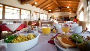 A breakfast setting with a white oval dish of scrambled eggs, a glass of orange juice, a plate with toast and kiwi, and a white cup on a table with a red napkin. - Hotel Antica Croce (Tenno)