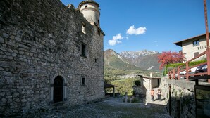 A stone building with a tower, a paved courtyard, and a mountain backdrop. - Hotel Antica Croce (Tenno)