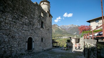 Un edificio de piedra con una torre, un patio empedrado y montañas al fondo.