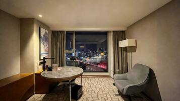 A hotel room with a bed, a desk, a chair, a window with a city view, and a patterned carpet.