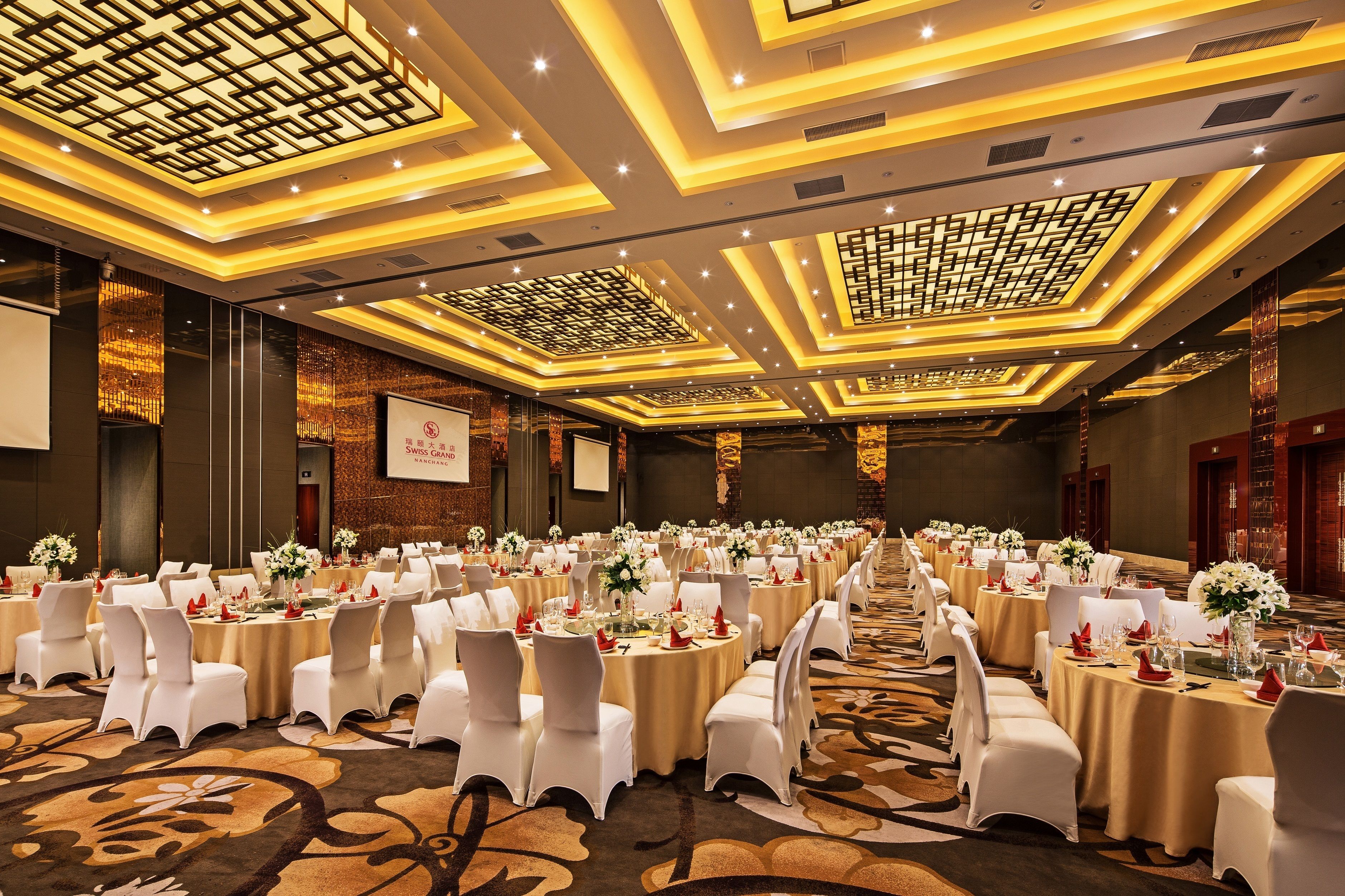 A banquet hall with round tables, white chairs, and floral centerpieces.