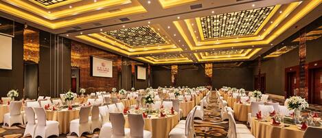 A banquet hall with round tables, white chairs, and floral centerpieces.