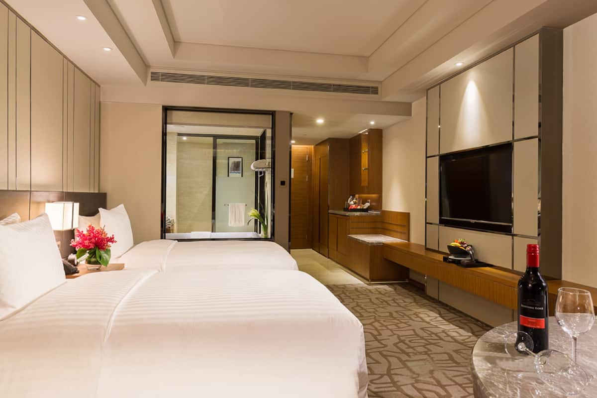 Ein Hotelzimmer mit zwei Betten, einem Fernseher, einer Minibar und einer Weinflasche auf einem Tisch.
