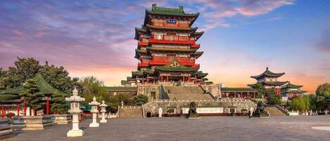 Una pagoda tradicional de varios niveles con una escalera que la lleva hacia arriba, rodeada por un patio con faroles de piedra y un cielo despejado.