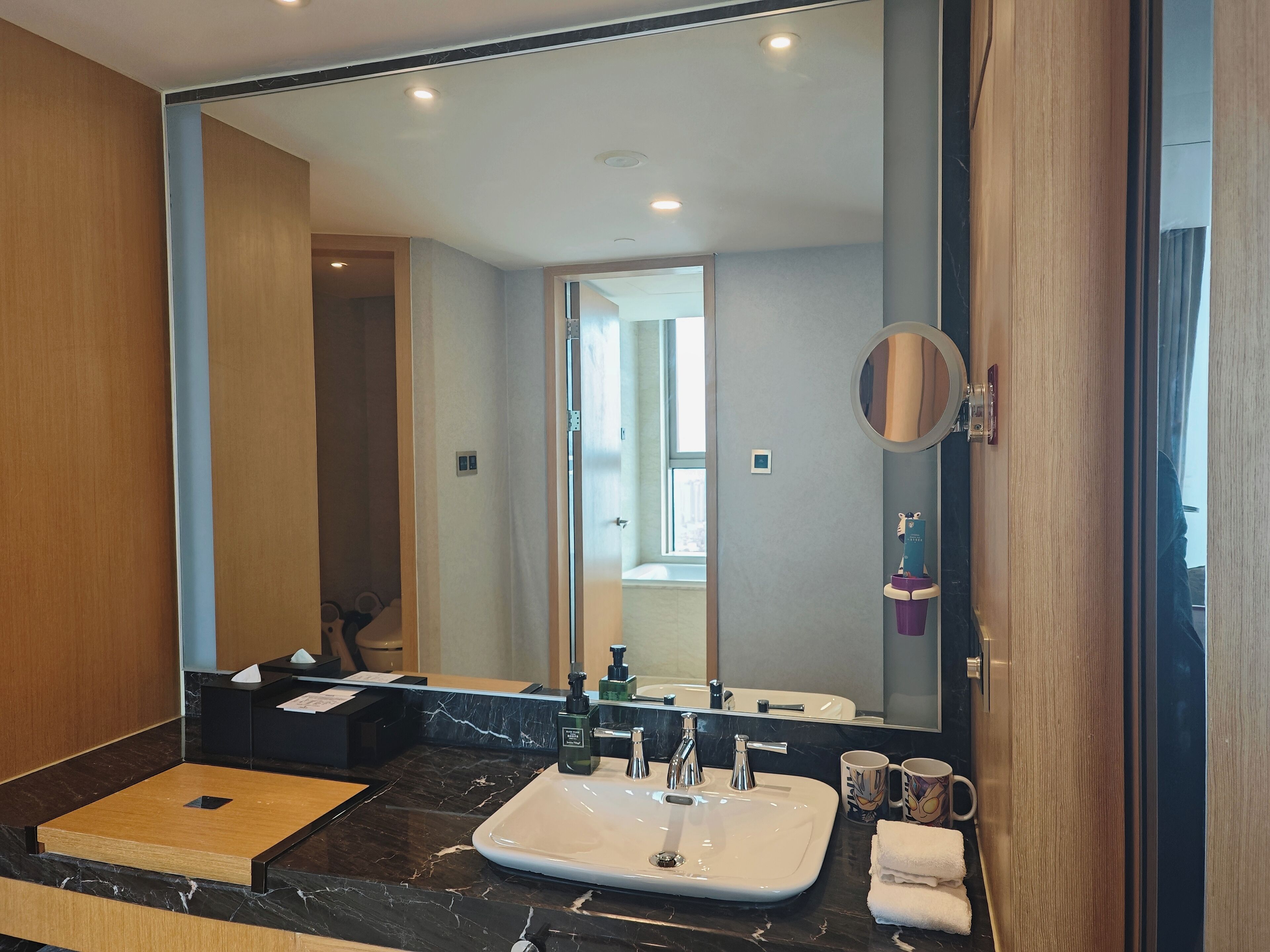 A modern bathroom with a large mirror, a white sink, and a marble countertop.