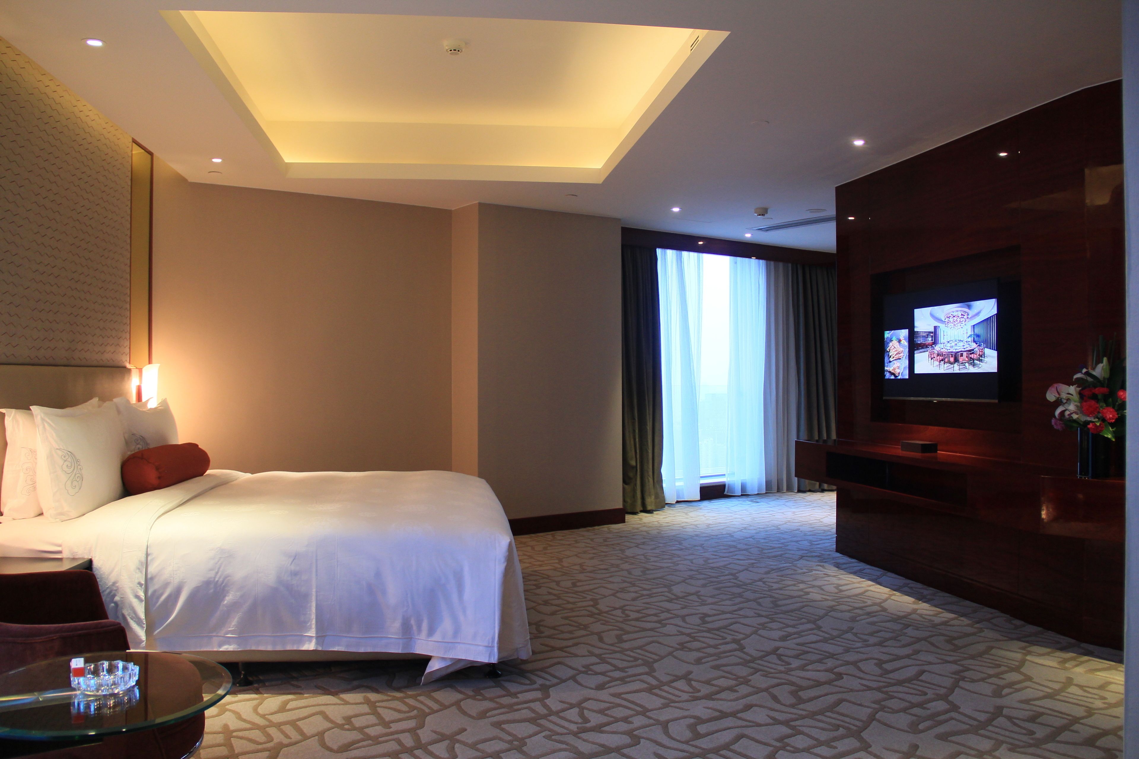 Quarto de hotel com uma cama grande, uma TV, uma mesa de centro de vidro e vista para o exterior pela janela.