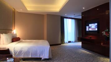 Quarto de hotel com uma cama grande, uma TV, uma mesa de centro de vidro e vista para o exterior pela janela.
