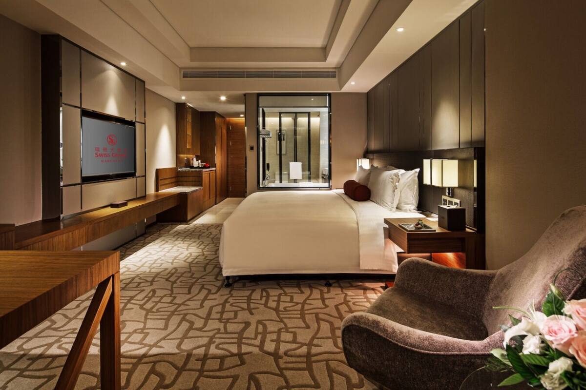 Ein Hotelzimmer mit einem großen Bett, einem Fernseher, einem Schreibtisch und einem Sessel.
