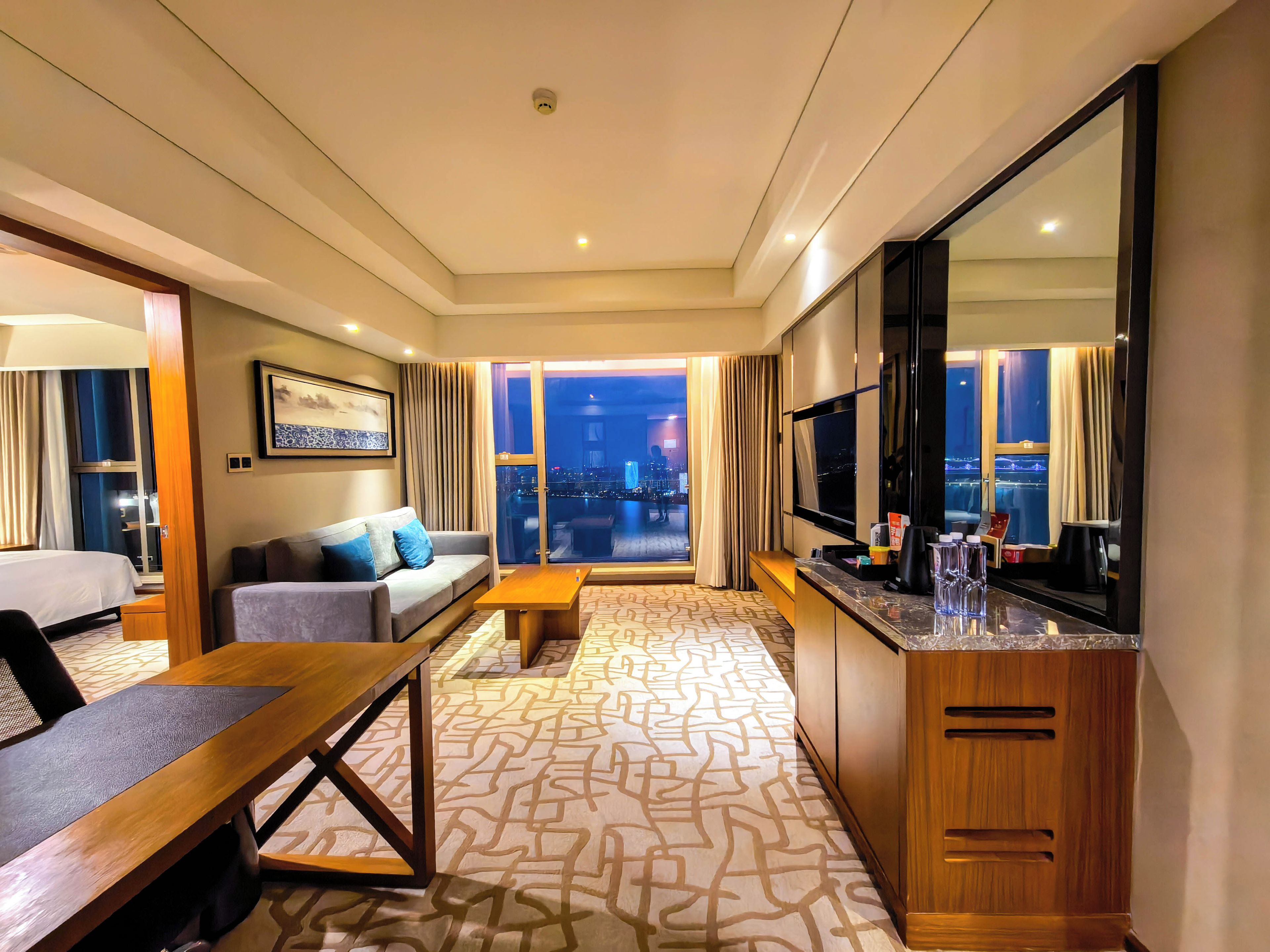 Habitación de hotel con sofá, mesa de comedor, televisión y vista a la ciudad desde la ventana.