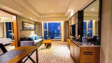 Habitación de hotel con sofá, mesa de comedor, televisión y vista a la ciudad desde la ventana.