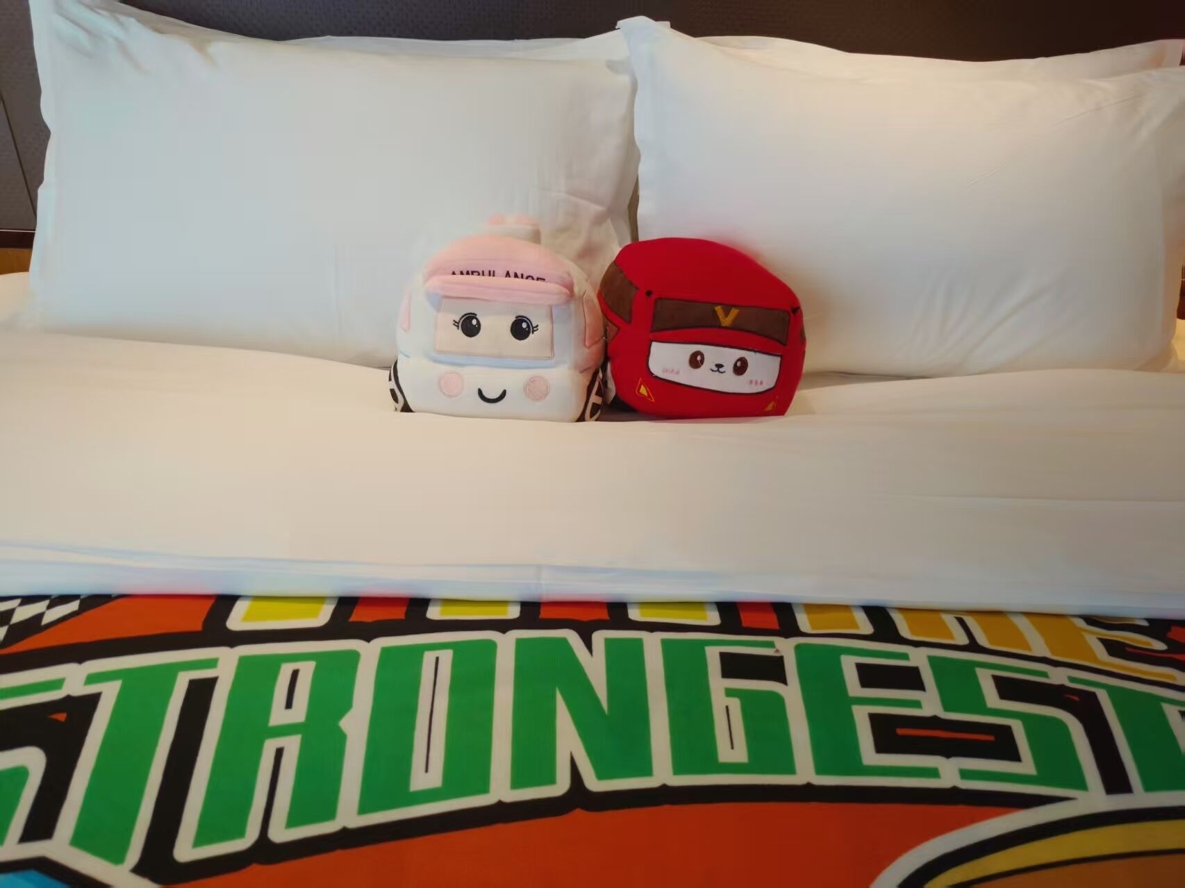 A bed with two pillows, one pink and one red, and a colorful bedspread with the word 'STRONGEST' visible.