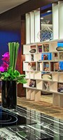 Un interior moderno con una mesa de mármol negro, un jarrón decorativo con flores moradas y una estantería blanca con diversos objetos.