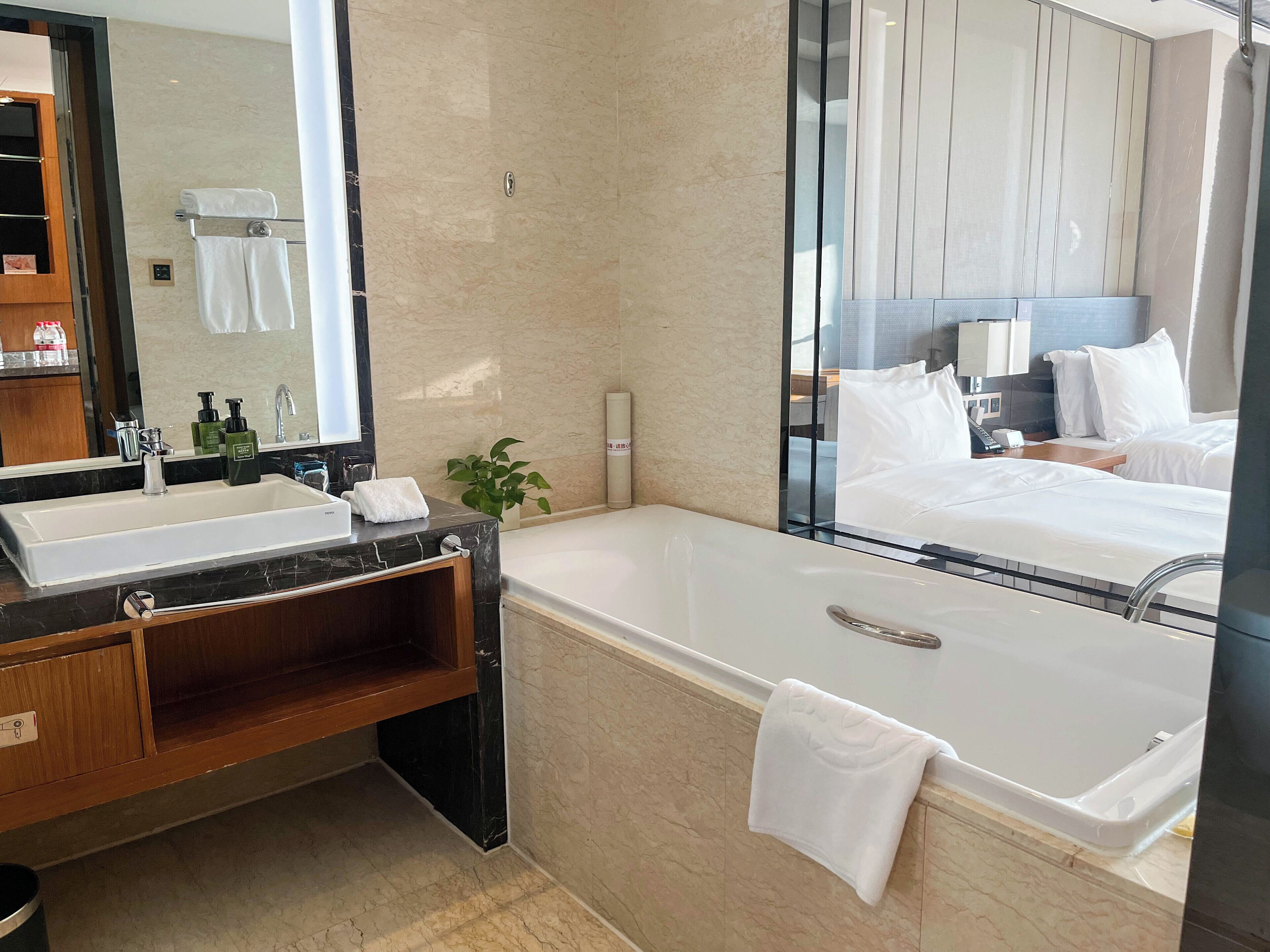 Un baño moderno con lavamanos de mármol, un espejo grande, una bañera y un mueble de tocador de madera.