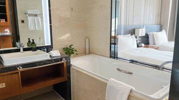 Un baño moderno con lavamanos de mármol, un espejo grande, una bañera y un mueble de tocador de madera.