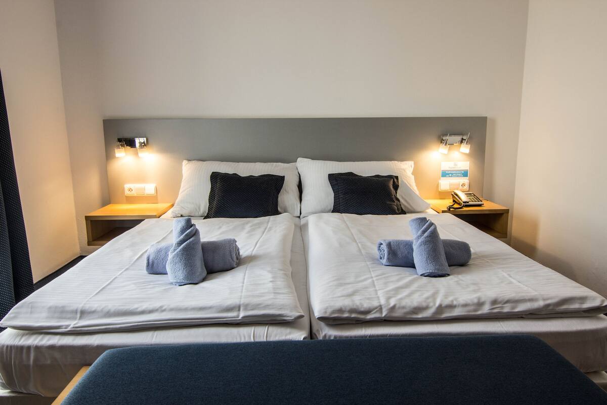 Una cama doble con dos almohadas y dos toallas, una mesita de noche con una lámpara y un teléfono.