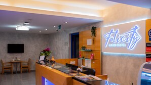 A hotel reception area with a wooden reception desk, a digital screen, and a neon sign for 'Felicity Carnit Hotel'. - Felicity Garni Hotel (Bratislava)