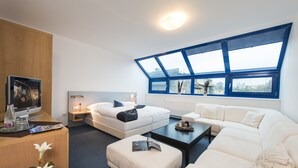 A modern hotel room with a large skylight, a flat-screen TV, a sofa, a coffee table, and a wooden cabinet. - Felicity Garni Hotel (Bratislava)