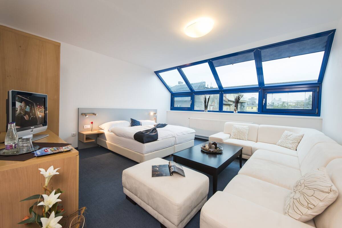 Una habitación de hotel moderna con un tragaluz grande, un televisor de pantalla plana, un sofá, una mesa de centro y un mueble de madera.