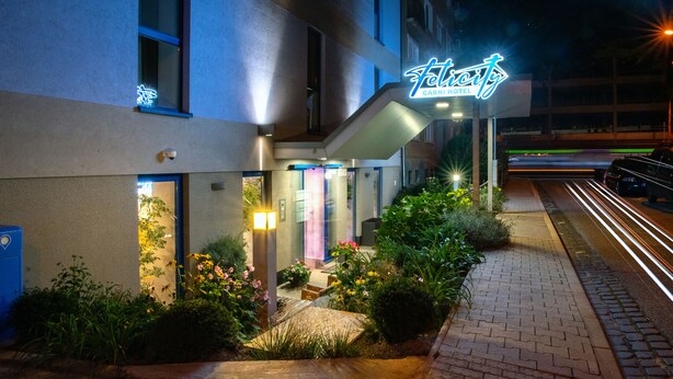A hotel entrance with a neon sign, a gated driveway, and a well-lit pathway. - Felicity Garni Hotel (Bratislava)