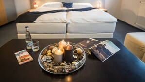 A neatly arranged hotel room with a bed, a table with candles, a bottle, and some magazines. - Felicity Garni Hotel (Bratislava)