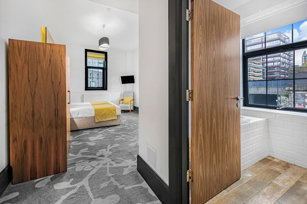 Una habitación de hotel moderna con una cama grande, un ventanal con vista a la ciudad y una puerta de madera.