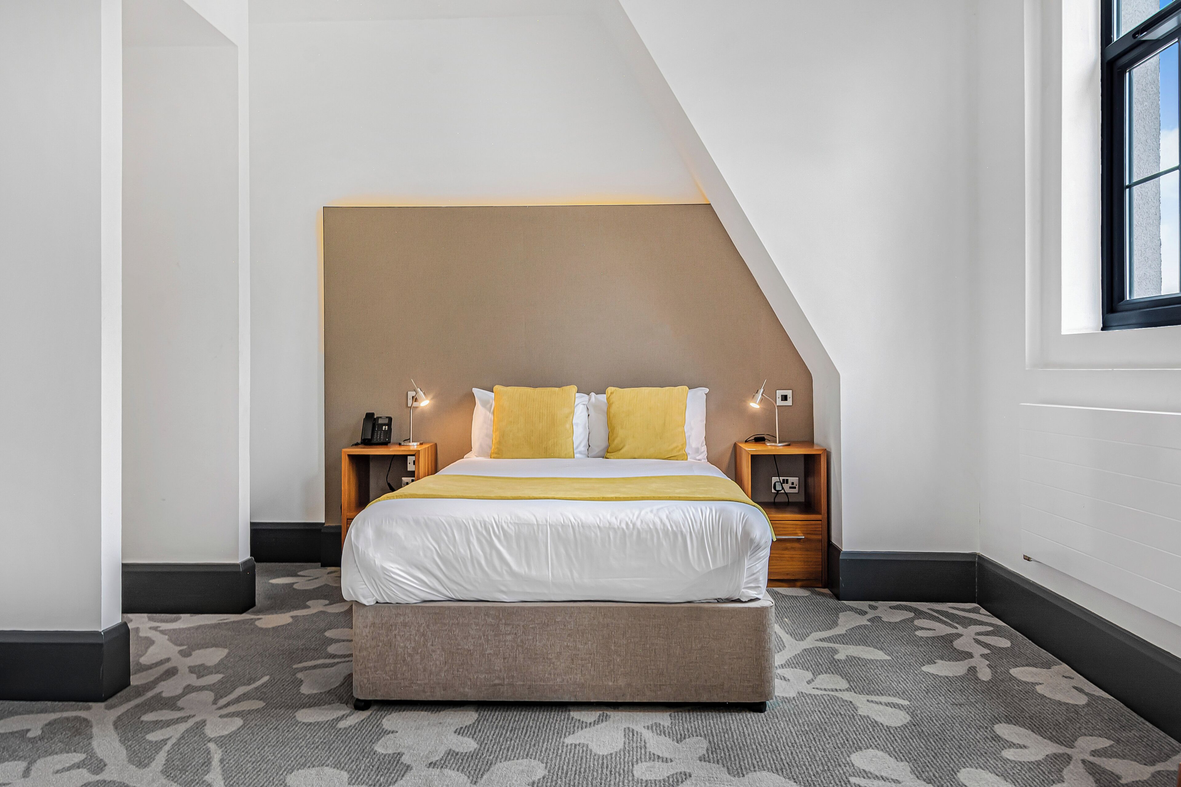 Un dormitorio moderno con una cama grande, un banco, dos mesitas de noche y una ventana.
