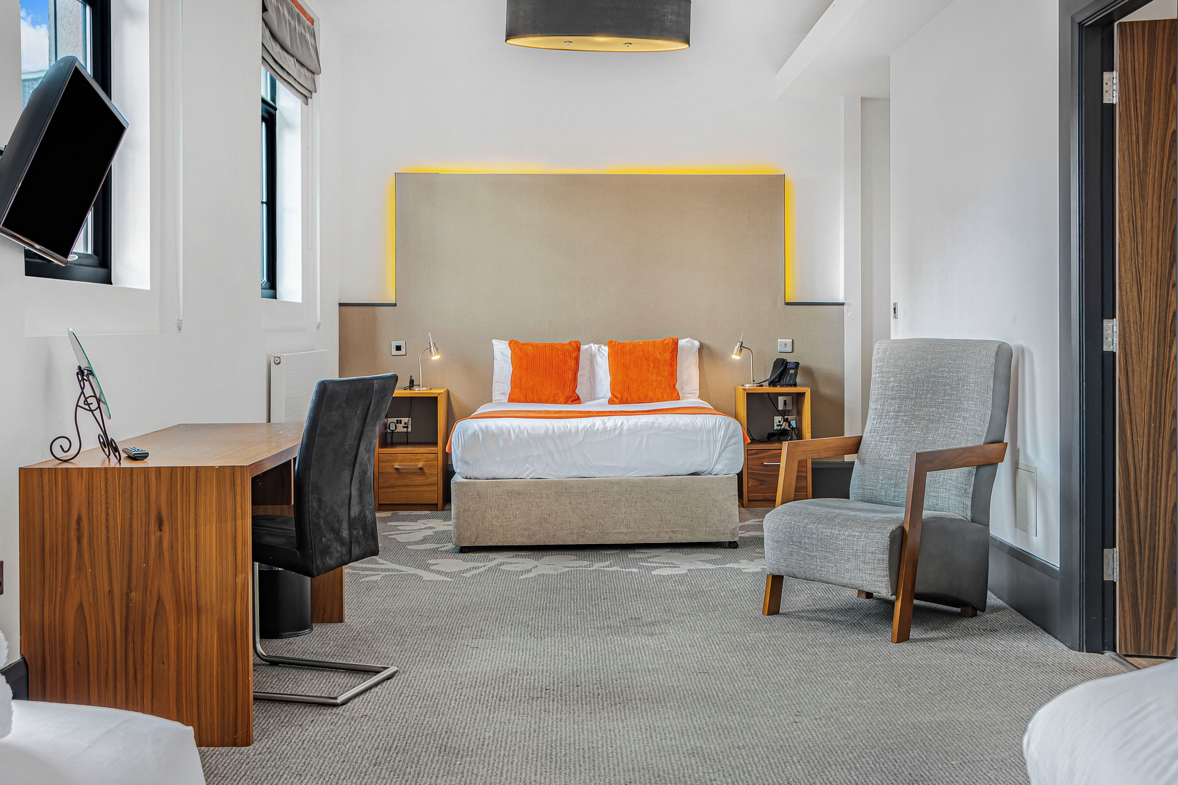 Una habitación de hotel moderna con una cama grande, un escritorio, una silla y un televisor montado en la pared.