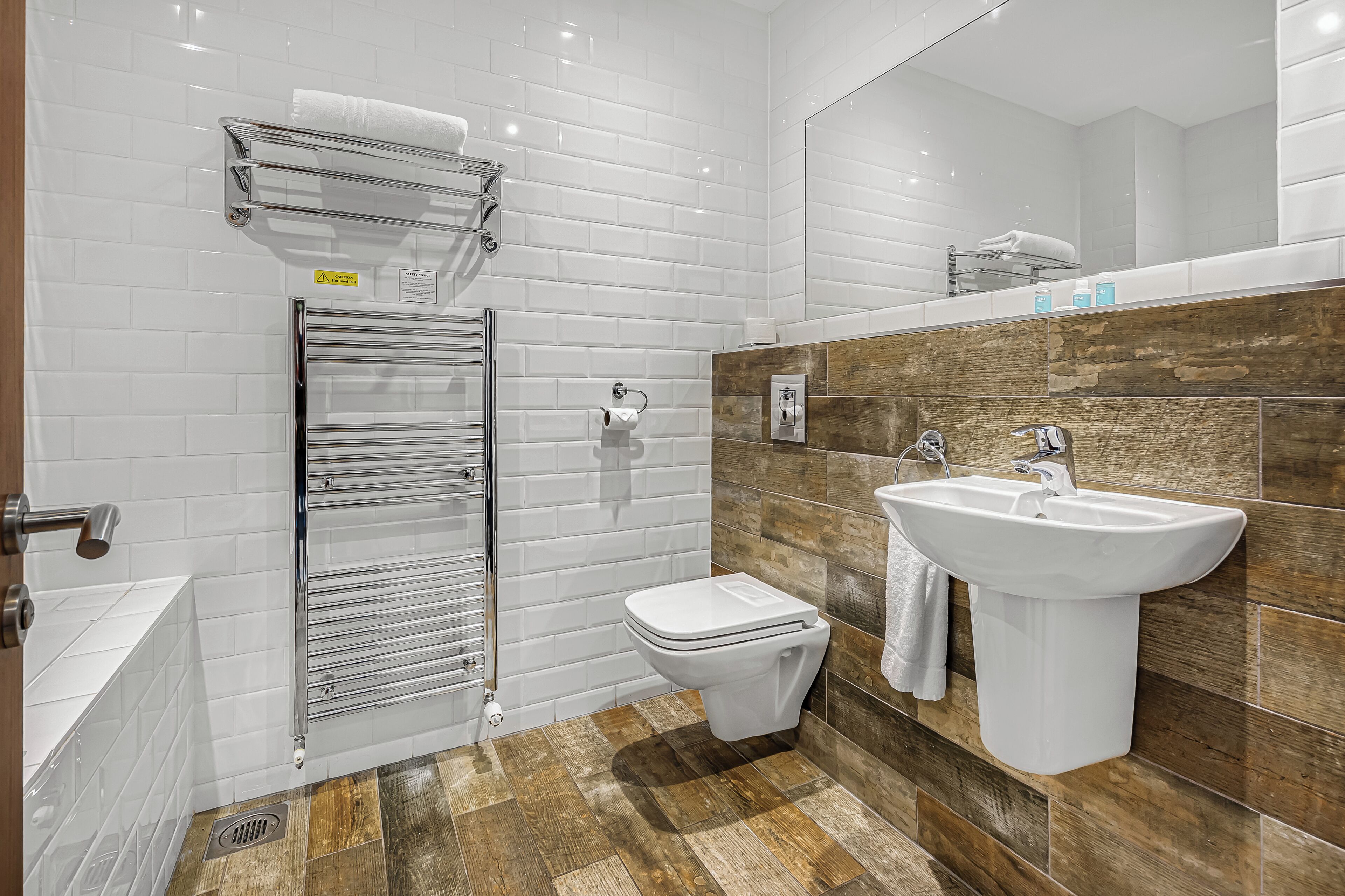 A modern bathroom with white tiled walls, a wooden accent wall, a white sink, and a toilet.