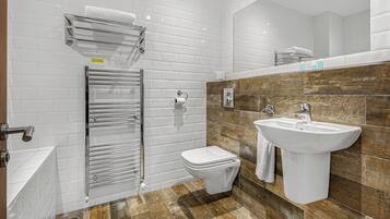 A modern bathroom with white tiled walls, a wooden accent wall, a white sink, and a toilet.