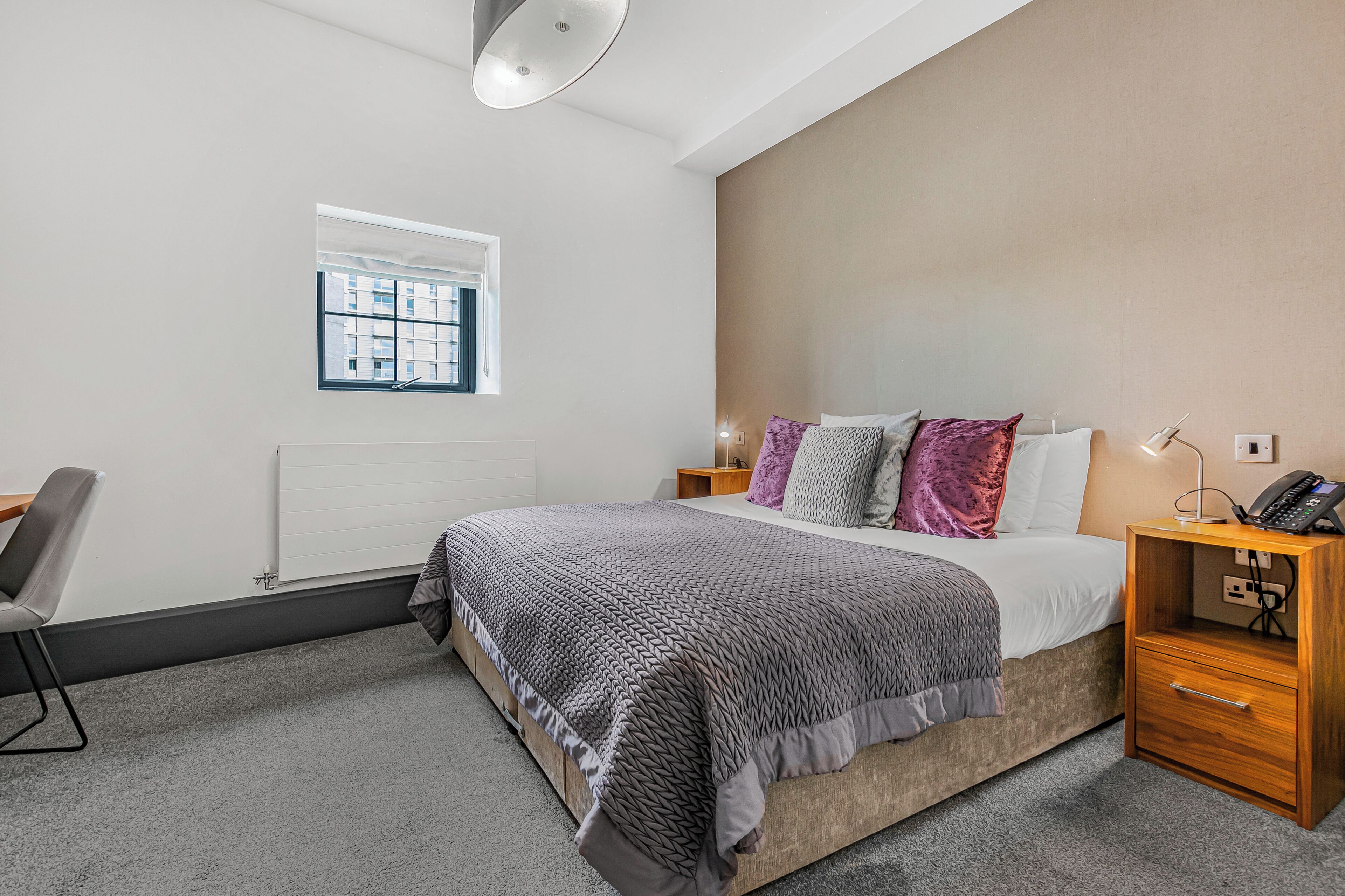 A bedroom with a bed, bedside table, lamp, and a window.
