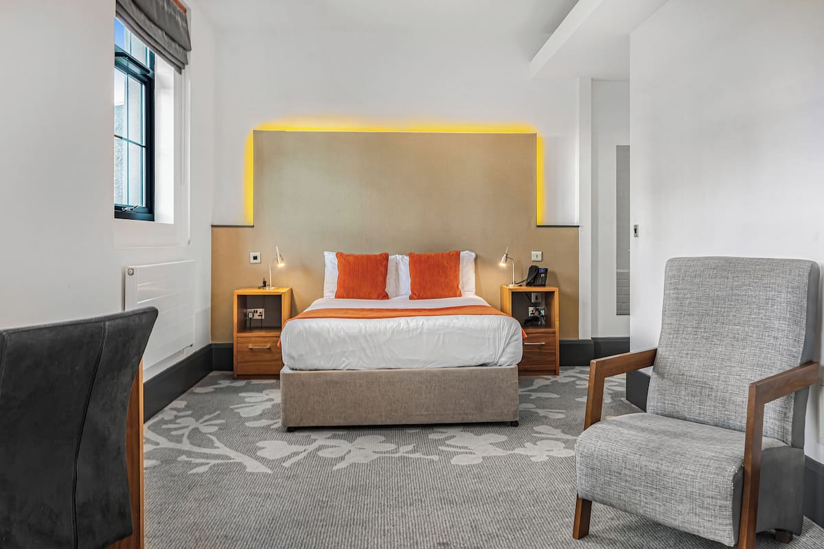 Una habitación de hotel con una cama, dos mesitas de noche, una silla y suelo cubierto de alfombra.