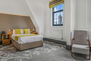 Un dormitorio con cama, mesitas de noche, una silla, ventana con vistas y un radiador.