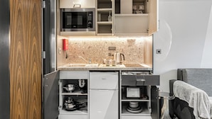 A compact kitchen with a microwave, sink, and a built-in refrigerator. - The Ainscow Hotel (Salford)