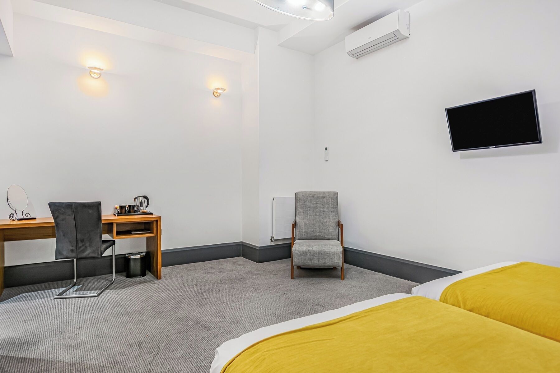 Une chambre d’hôtel avec un lit, un bureau, une chaise, une télévision et un radiateur.
