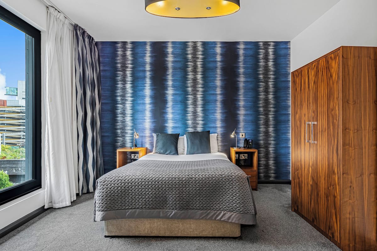 Un dormitorio moderno con una cama grande, vistas a la ciudad y un armario de madera.