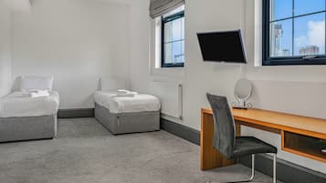 Ein Hotelzimmer mit zwei Betten, einem Schreibtisch, einem Stuhl, einem Fernseher und einem Fenster mit Blick auf die Stadt.