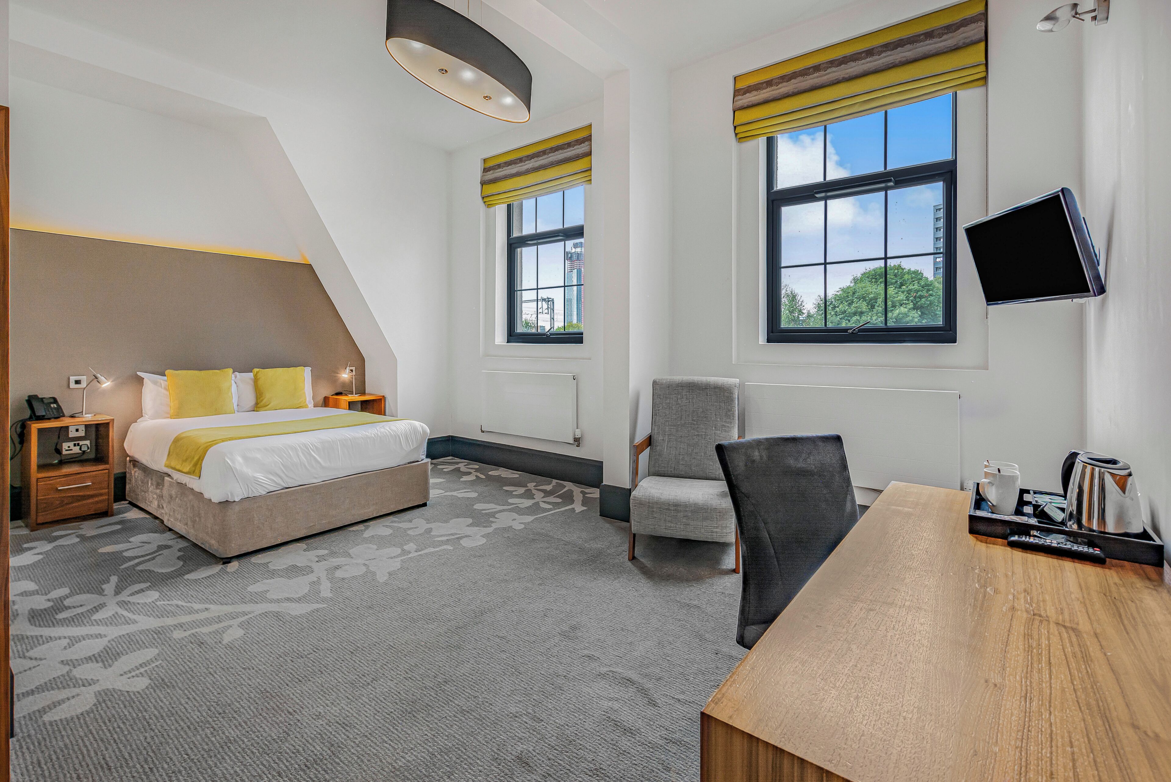 A modern hotel room with a bed, a desk, a chair, and a TV.