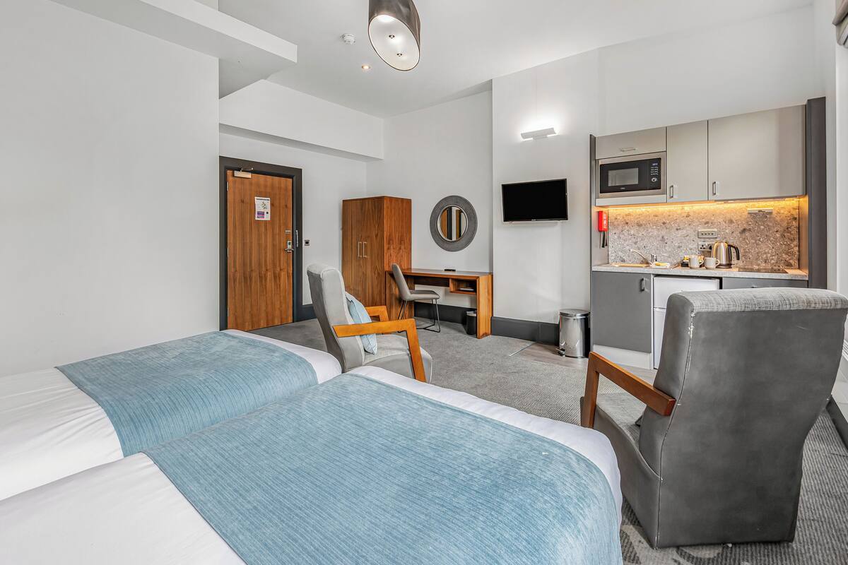 Habitación de hotel con dos camas, un escritorio, una silla, un televisor, microondas y una pequeña kitchenette.