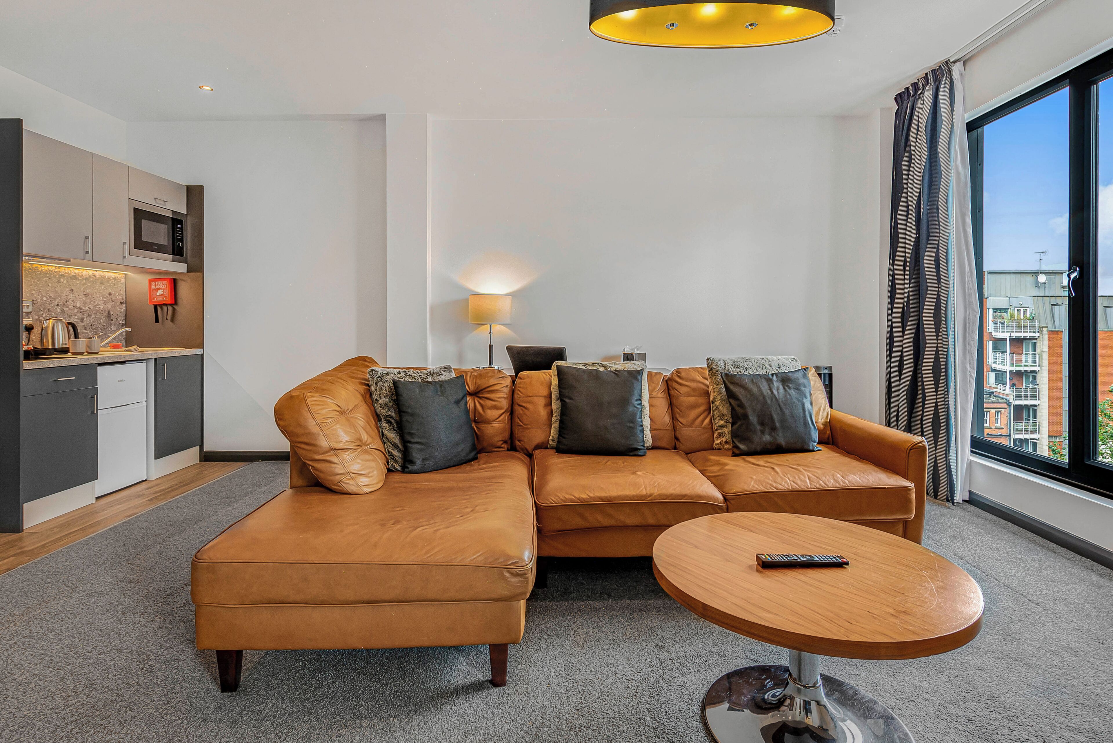 A modern living room with a sectional sofa, a coffee table, and a view of the city through large windows.