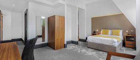 A modern hotel room with a large bed, a desk, and a wardrobe.