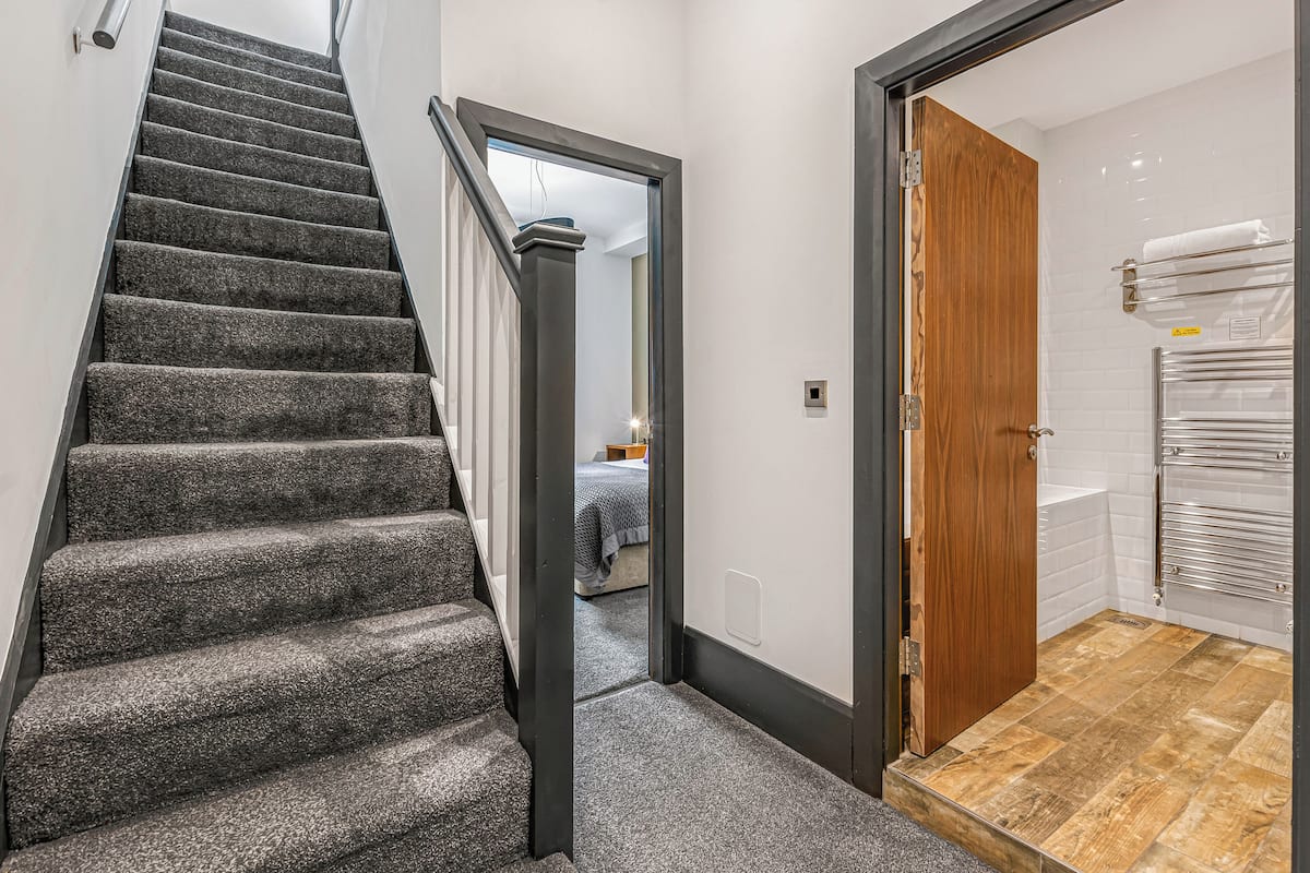 Una escalera conduce a un dormitorio con una puerta de madera y un baño con un perchero.