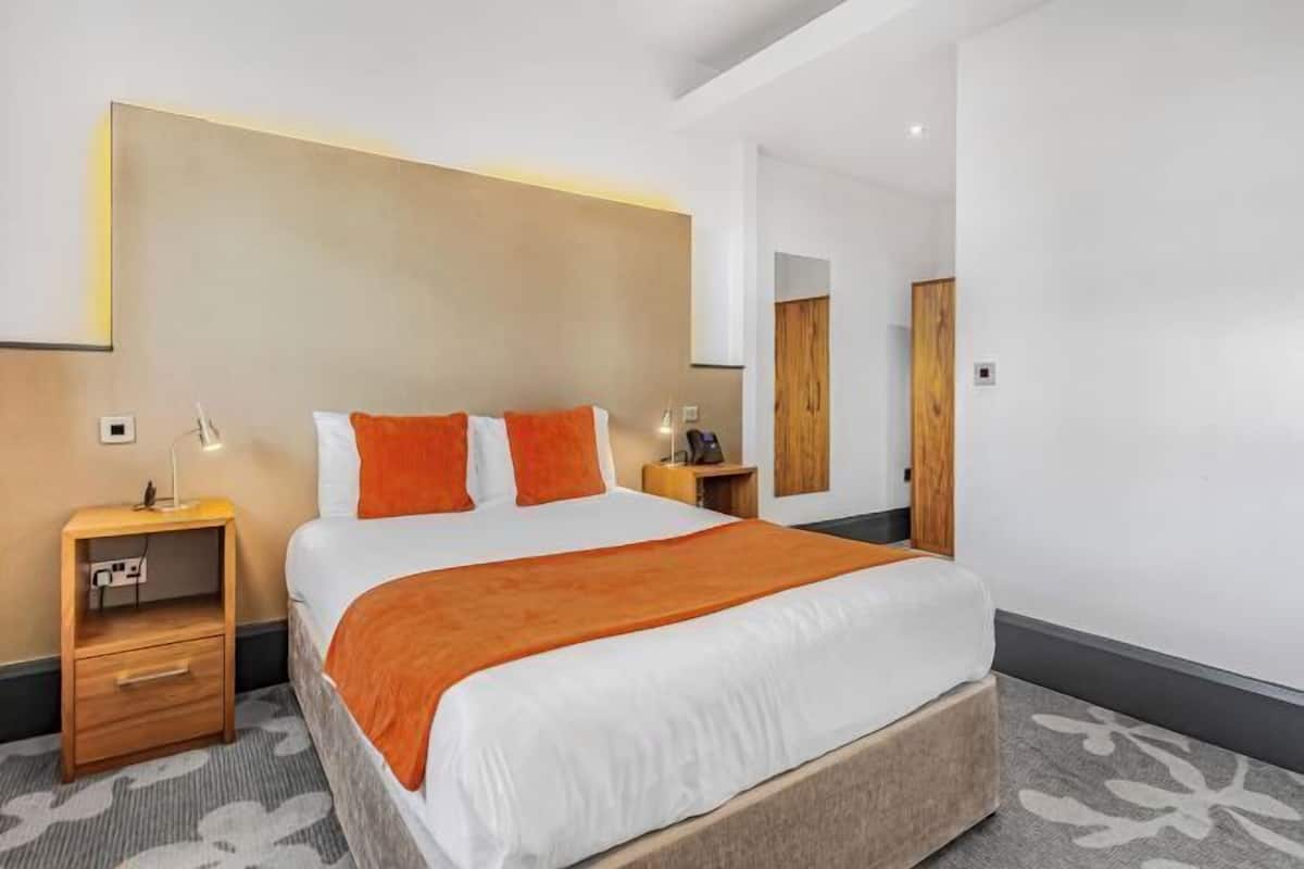 Una habitación de hotel moderna con una cama grande, una mesita de noche, un armario de madera y un espejo.