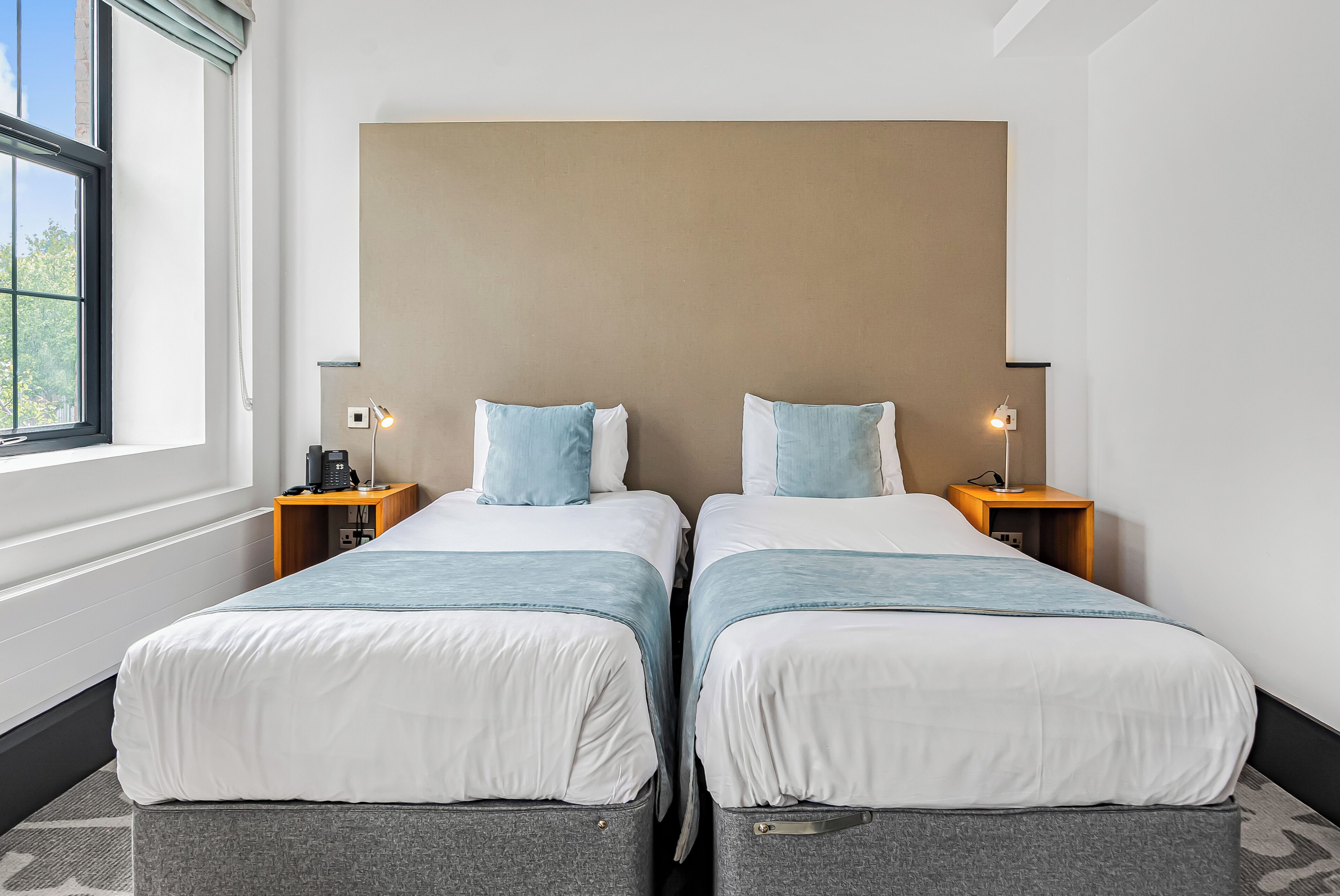 A hotel room with two beds, a large window, and a neutral color scheme.