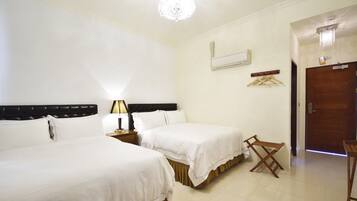 Habitación de hotel con dos camas, una mesita de noche con lámpara, un perchero y una puerta.